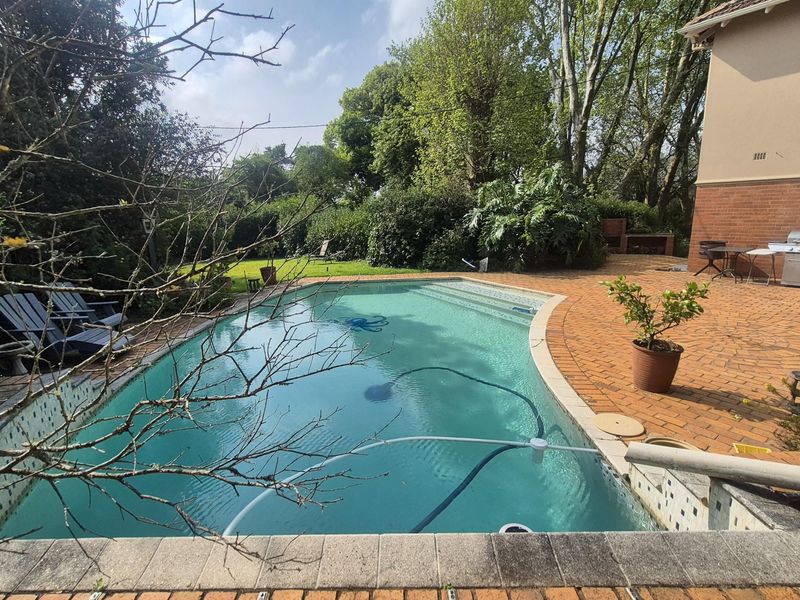 Outdoor pool area featuring a swimming pool with steps, brick paved patio, and a built-in brick braai, set within a landscaped garden.