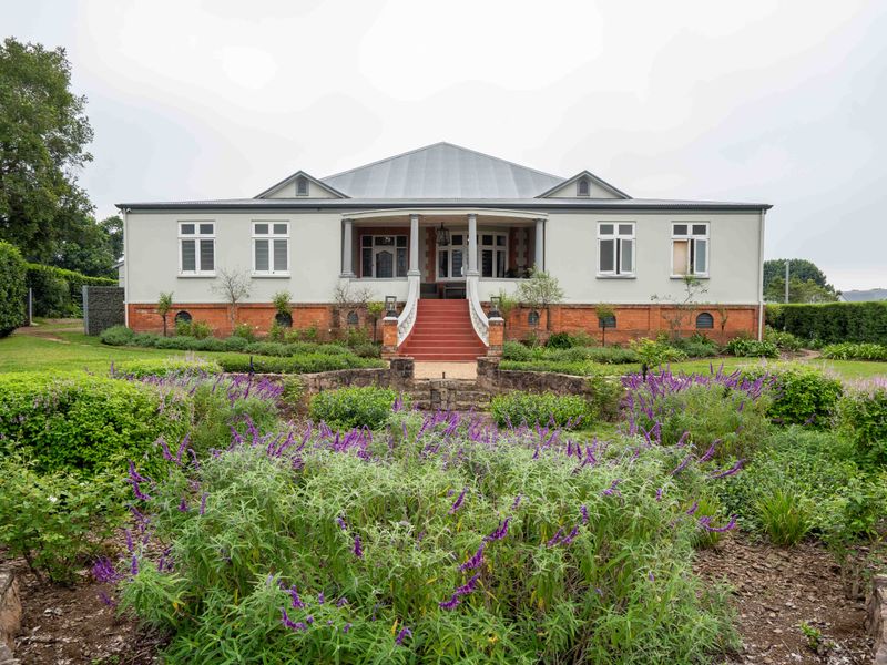 A well-maintained rear elevation of a classic home featuring a covered porch, brick base, and a beautifully landscaped garden with stone retaining walls.