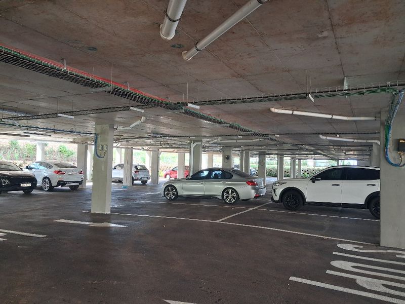 A covered basement parking garage featuring concrete structural elements, exposed utility services, and marked parking bays.