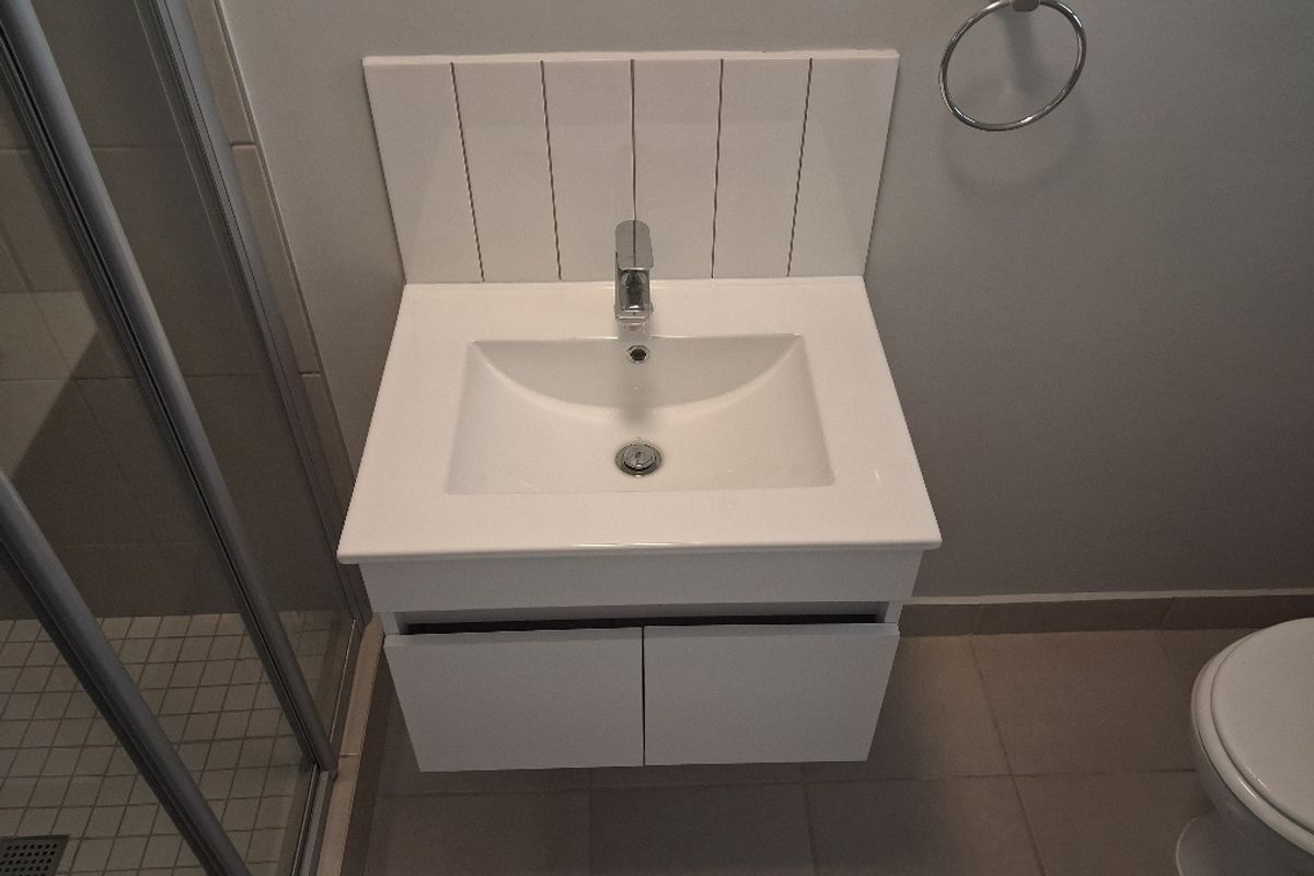 Modern bathroom featuring a wall-mounted vanity with a ceramic basin, chrome mixer tap, tiled splashback, and a glass-enclosed shower.