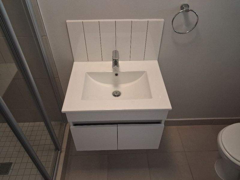 Modern bathroom featuring a wall-mounted vanity with a ceramic basin, chrome mixer tap, tiled splashback, and a glass-enclosed shower.