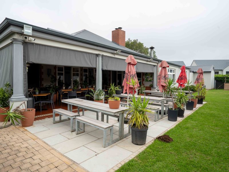 A spacious covered patio area featuring paved flooring, structural columns, and retractable blinds, providing a seamless transition to the adjacent garden space.