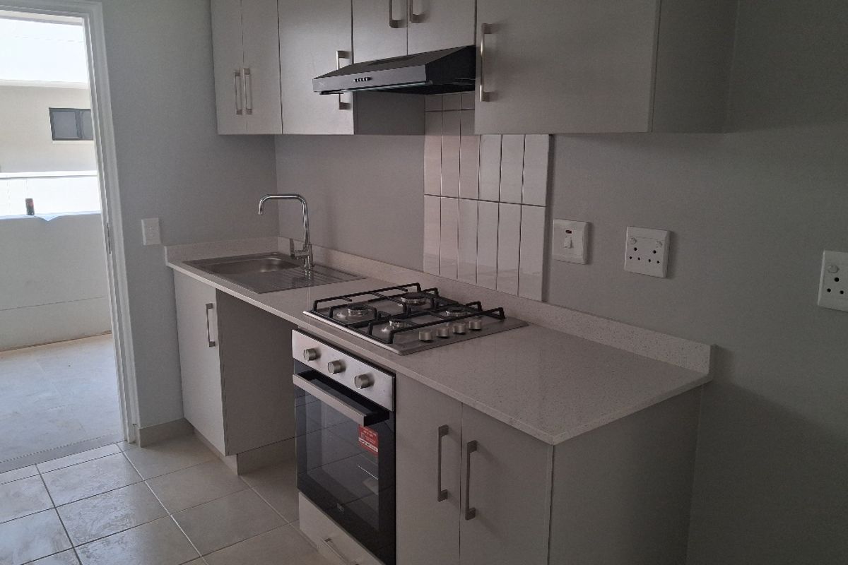 A modern, clean kitchen featuring light grey cabinetry, stone countertops, a gas hob, built-in oven, and stainless steel sink.