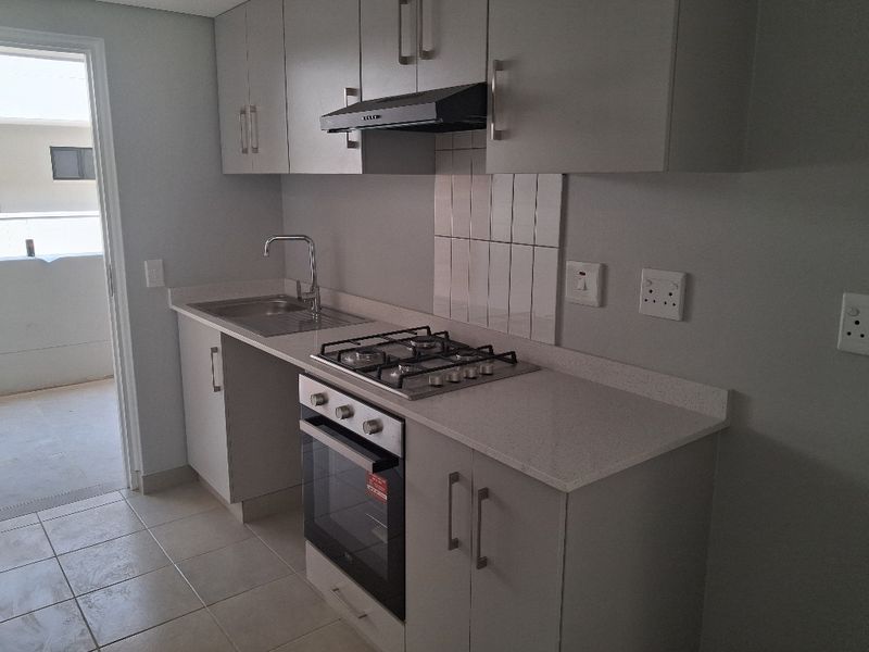 A modern, clean kitchen featuring light grey cabinetry, stone countertops, a gas hob, built-in oven, and stainless steel sink.