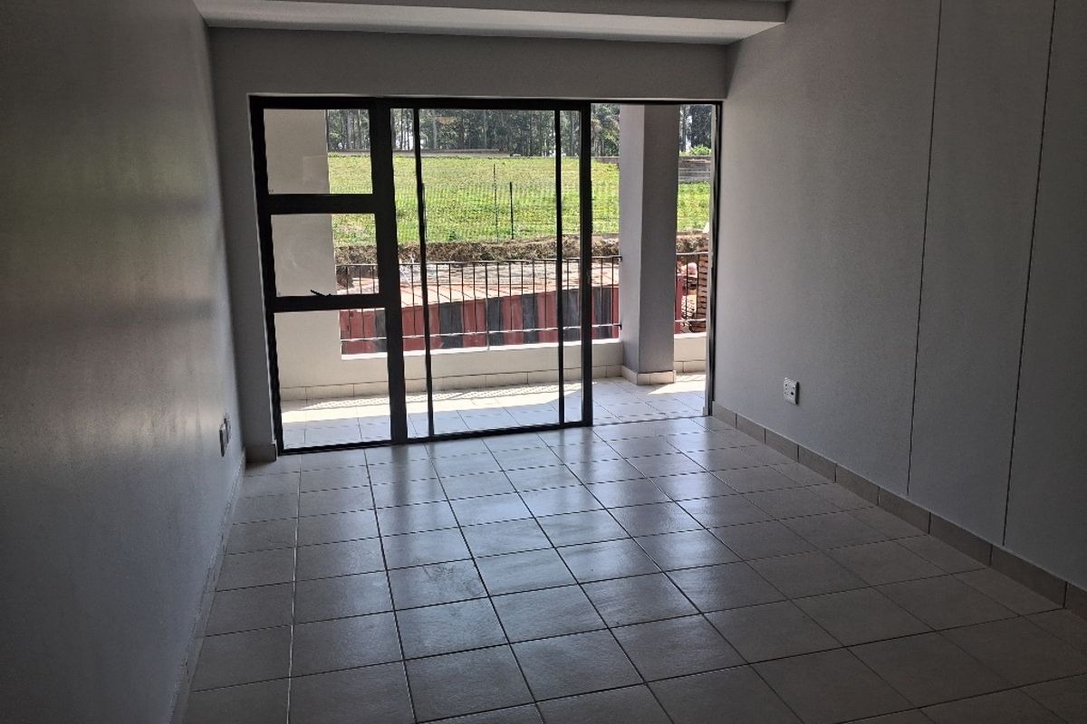 An empty, well-lit living area featuring neutral tiled flooring and a large sliding glass door providing direct access to an outdoor balcony.