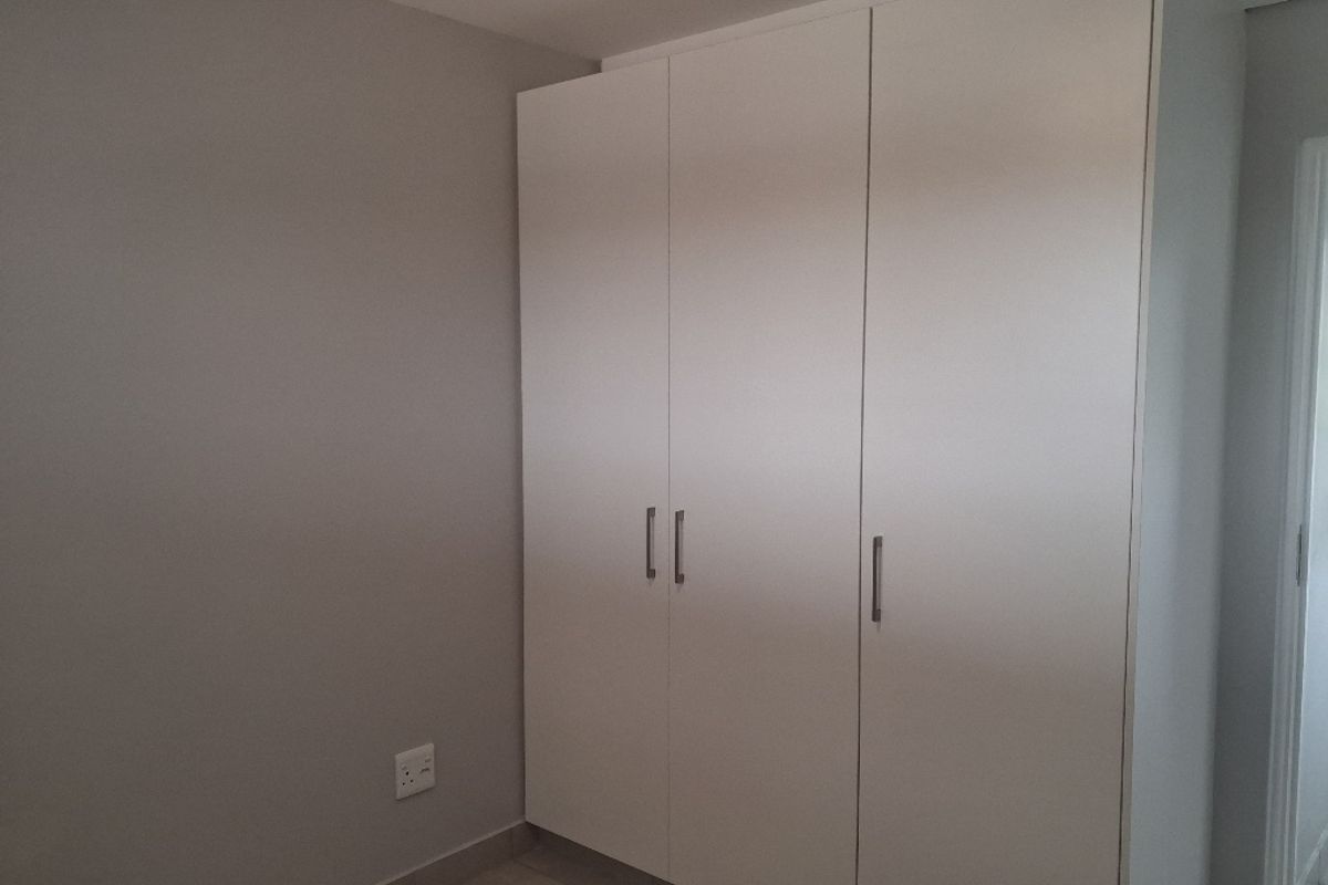 A clean, neutral bedroom featuring a modern built-in wardrobe with white cabinetry and smooth finishes.