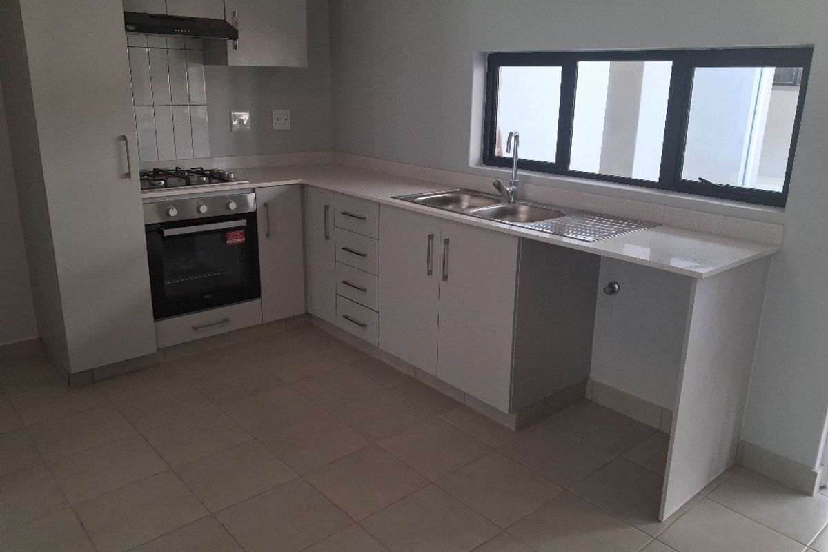 Modern kitchen featuring light-toned cabinetry, stone countertops, a built-in gas hob, oven, extractor fan, and a double sink with tiled flooring.