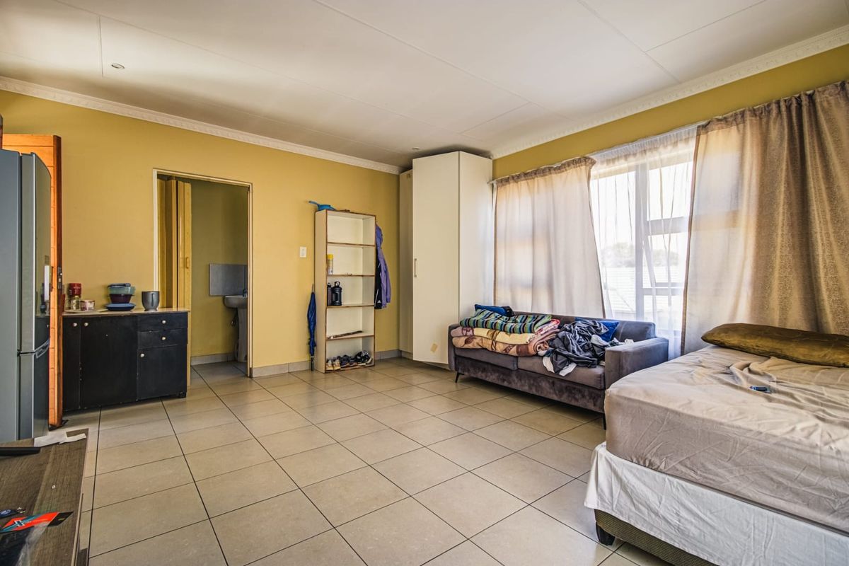 Spacious bedroom featuring tiled flooring, built-in storage, and large windows allowing for natural light, with an adjoining en-suite bathroom.