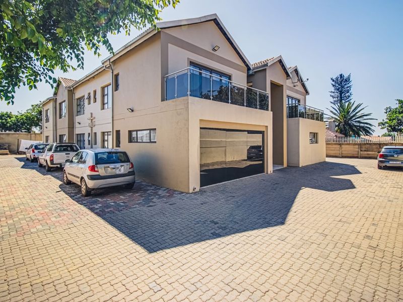 Front elevation of a modern multi-story residential property featuring a paved driveway, integrated garage, and upper-level balconies with glass balustrades.