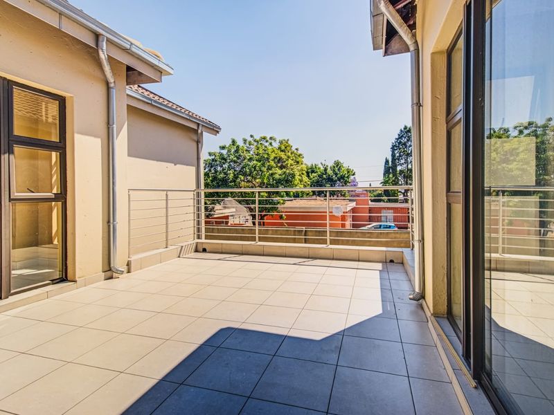 A spacious, tiled balcony featuring a modern stainless steel balustrade and large sliding glass doors, offering an open outdoor living area.