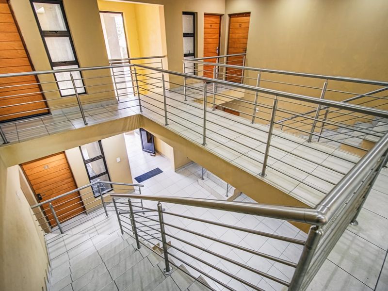 A multi-level interior hallway featuring tiled flooring, a stainless steel balustrade, and multiple wooden unit doors.