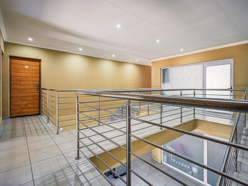 A spacious, well-lit upper-level landing featuring modern stainless steel balustrades, tiled flooring, and access to multiple rooms.