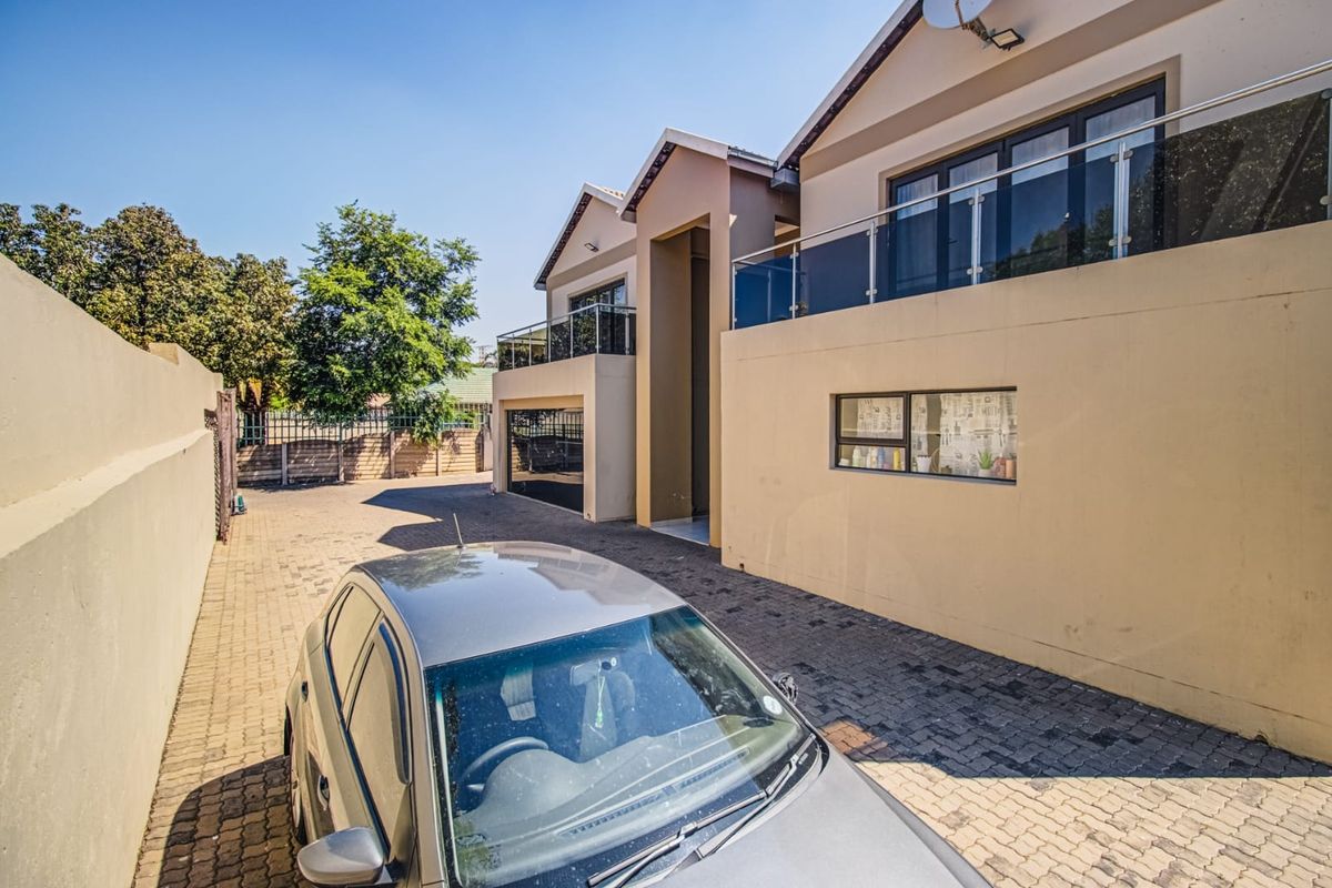 A modern double-story residential exterior featuring a paved driveway, integrated garage, and upper-level balconies with glass balustrades.