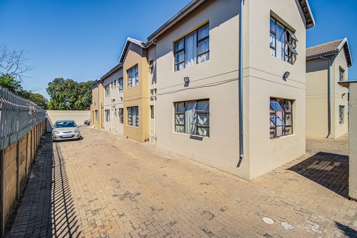 Side view of a multi-story residential building featuring paved driveway access, perimeter security fencing, and exterior wall-mounted lighting.