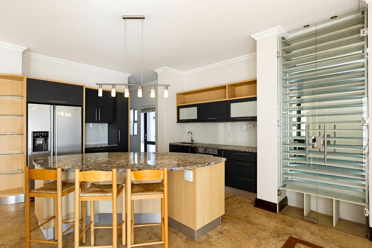 Modern kitchen featuring a large granite-topped island, dark cabinetry with light wood accents, and a unique glass louvered door entry.