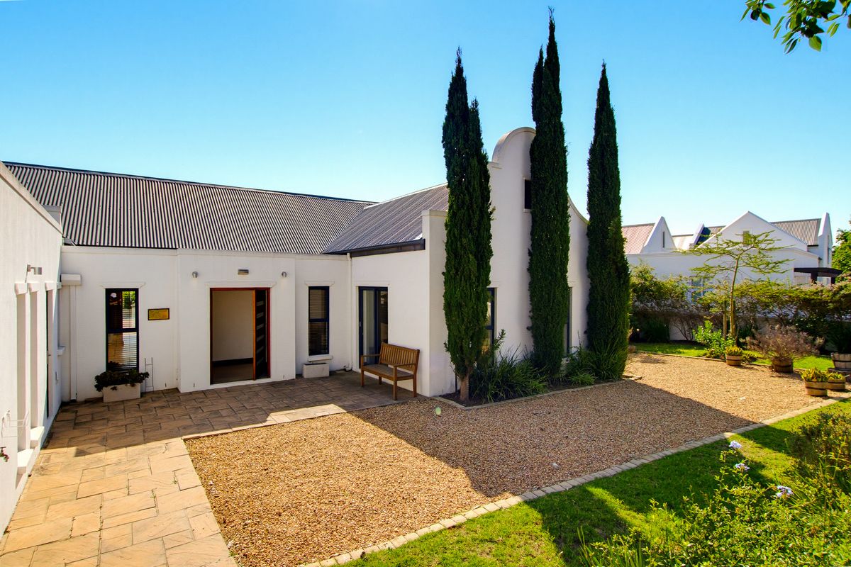 A well-maintained rear exterior featuring a classic gabled facade, paved patio area, and landscaped garden with gravel pathways.