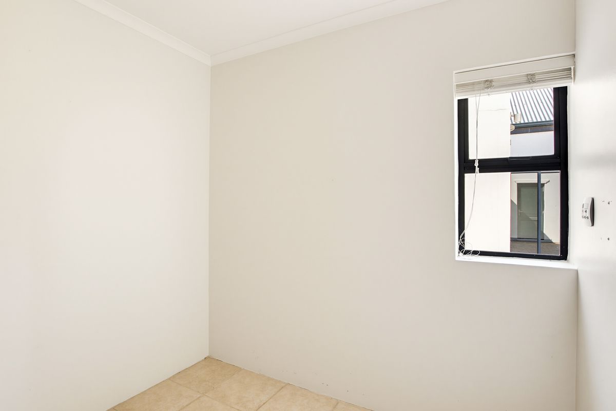 A clean, empty bedroom featuring neutral tiled flooring, a modern aluminium window frame with a fitted blind, and a simple, well-maintained interior finish.