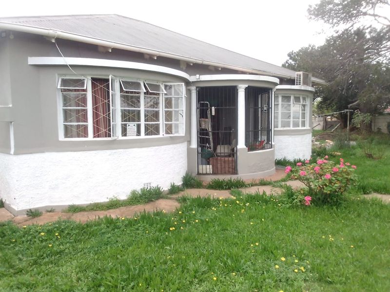 Rear view of a house featuring a corrugated metal roof, security-barred windows, and a small patio area set within an overgrown garden.