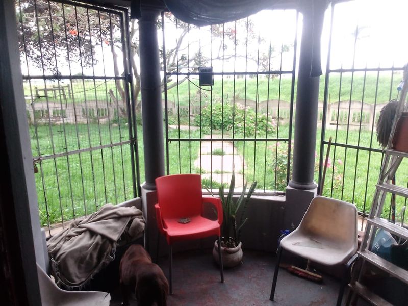 A covered patio area featuring concrete columns and security bars, overlooking a garden space. The area requires maintenance and cosmetic updates.