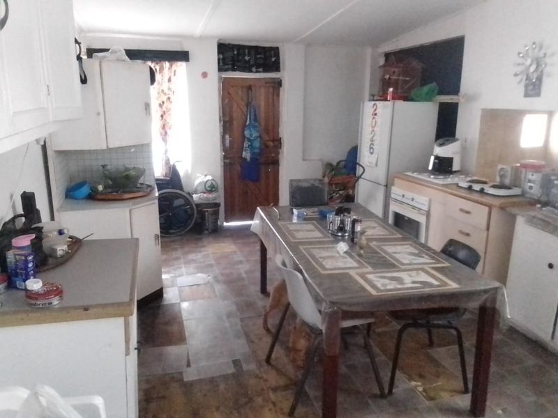 Open-plan kitchen and dining area featuring dated cabinetry, built-in oven and hob, and tiled flooring in need of refurbishment.