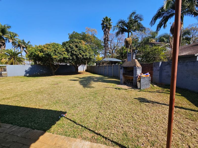 Spacious backyard garden featuring a built-in brick braai area, perimeter walling, and mature trees.