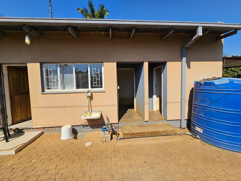 Rear exterior view of the property featuring a paved patio area, external sink, and a large water storage tank.