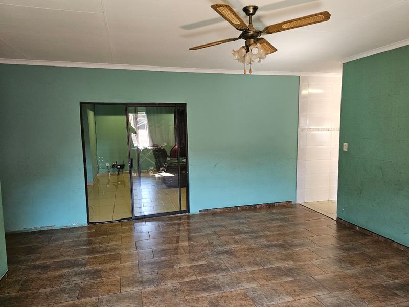 An empty living room featuring tiled flooring, a ceiling fan, and a sliding glass door leading to an adjacent space.