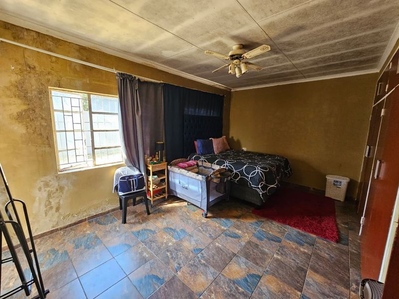 Bedroom featuring tiled flooring, a ceiling fan, and built-in wardrobe. The room requires significant cosmetic attention due to visible wall and ceiling damage.
