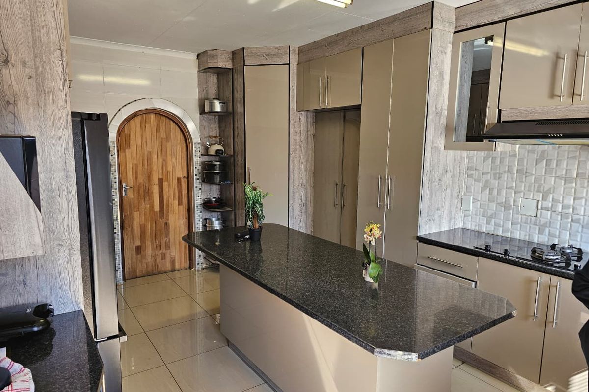 Modern kitchen featuring granite countertops, a central island, built-in cabinetry, tiled backsplash, and an integrated hob with extractor fan.