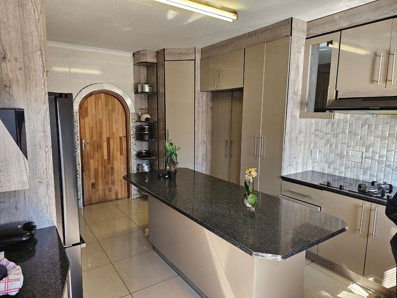 Modern kitchen featuring granite countertops, a central island, built-in cabinetry, tiled backsplash, and an integrated hob with extractor fan.