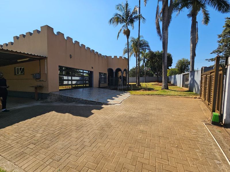 Front exterior view of the property featuring a paved driveway, covered carport, and a distinctive parapet wall design with surrounding garden space.