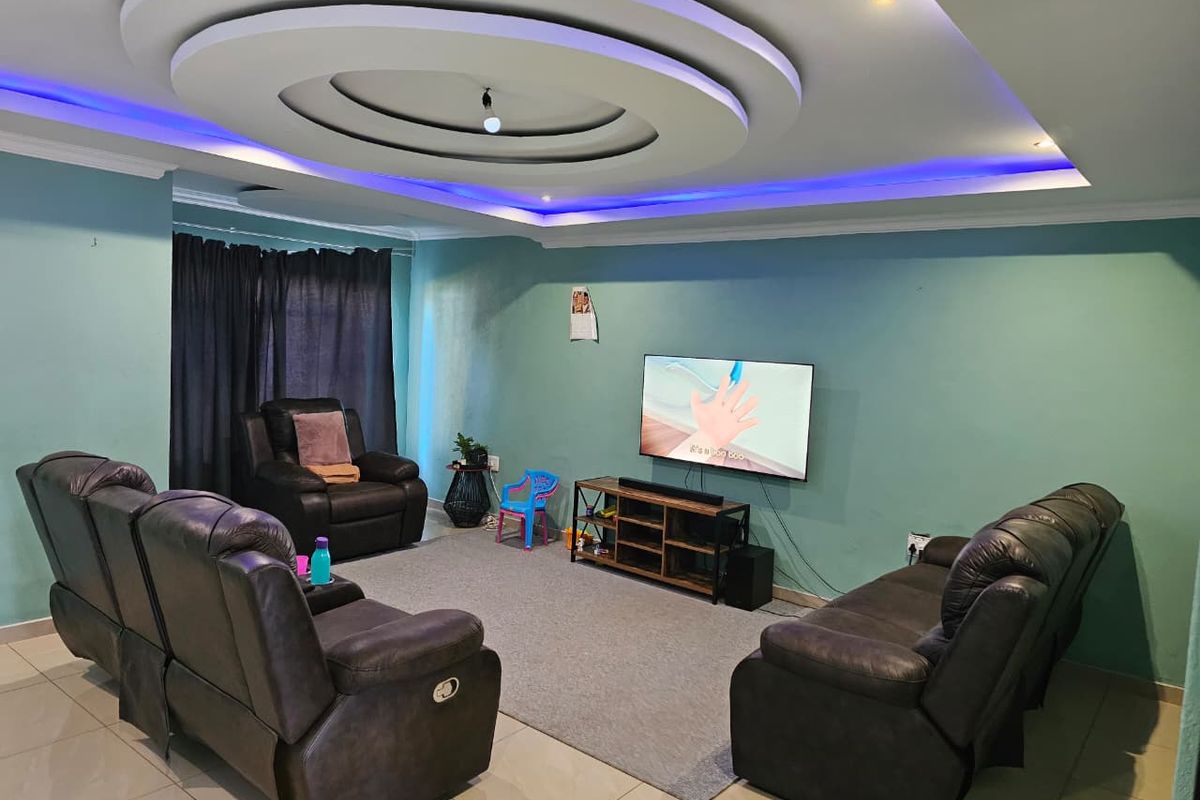 A spacious living room featuring a decorative recessed ceiling with integrated LED cove lighting and neutral tiled flooring.