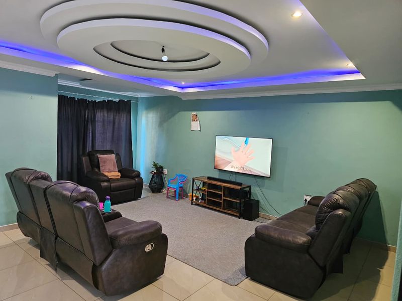 A spacious living room featuring a decorative recessed ceiling with integrated LED cove lighting and neutral tiled flooring.