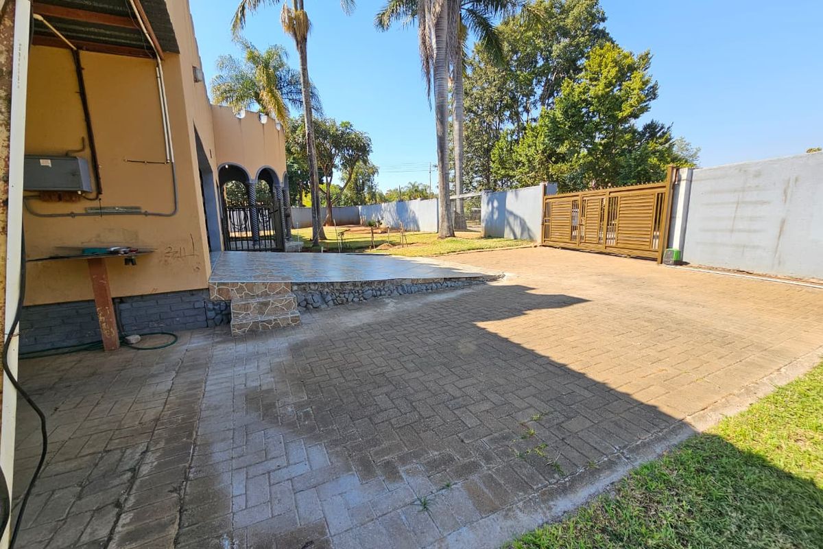 Rear exterior view featuring a paved driveway, tiled patio area, boundary wall, and metal sliding gate.