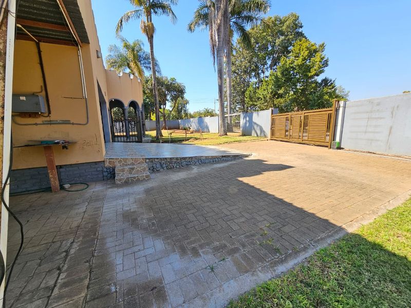 Rear exterior view featuring a paved driveway, tiled patio area, boundary wall, and metal sliding gate.