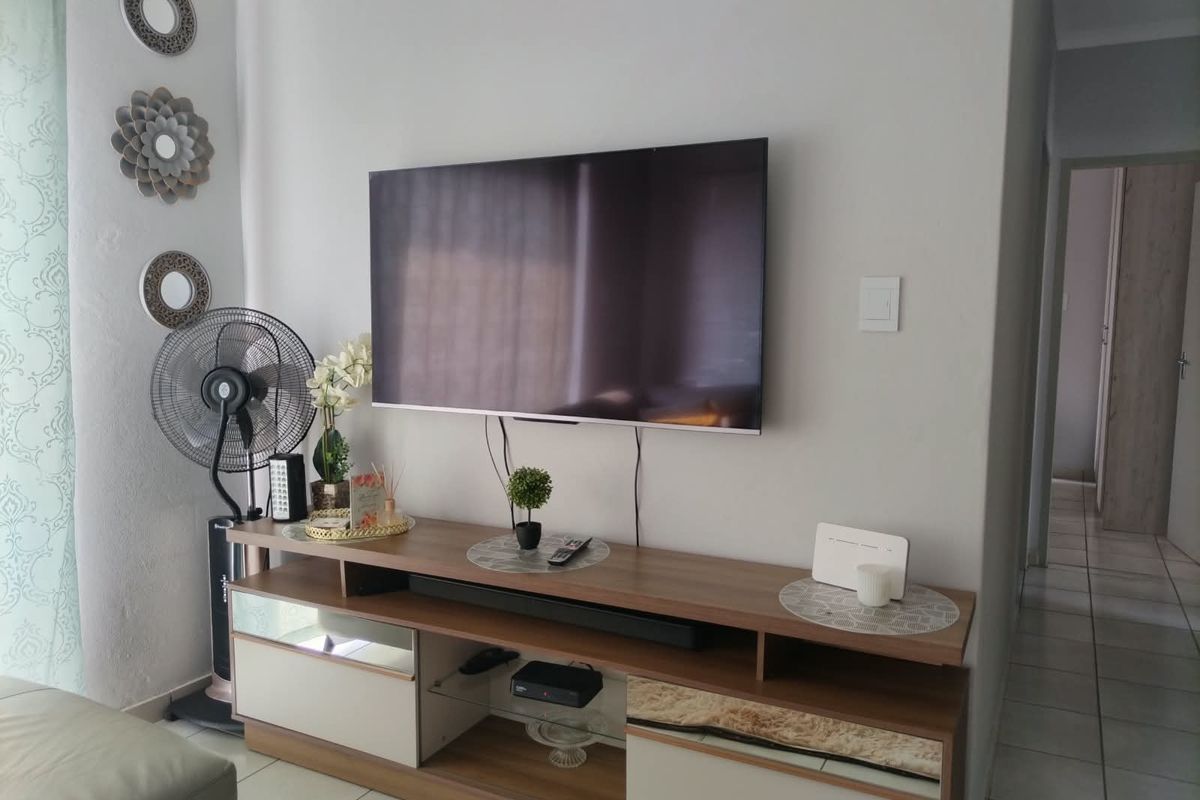 A living room area featuring tiled flooring and a wall-mounted television setup with neutral wall finishes.