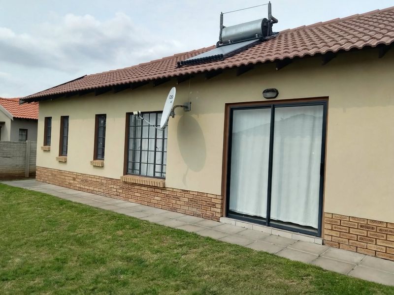 Rear view of the house featuring a tiled roof with a solar water heater, brick-accented exterior walls, and a sliding glass door leading to the garden.