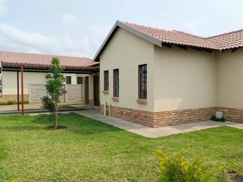 A view of the rear exterior of the house featuring a tiled roof, brick accents, a paved walkway, and an attached carport.
