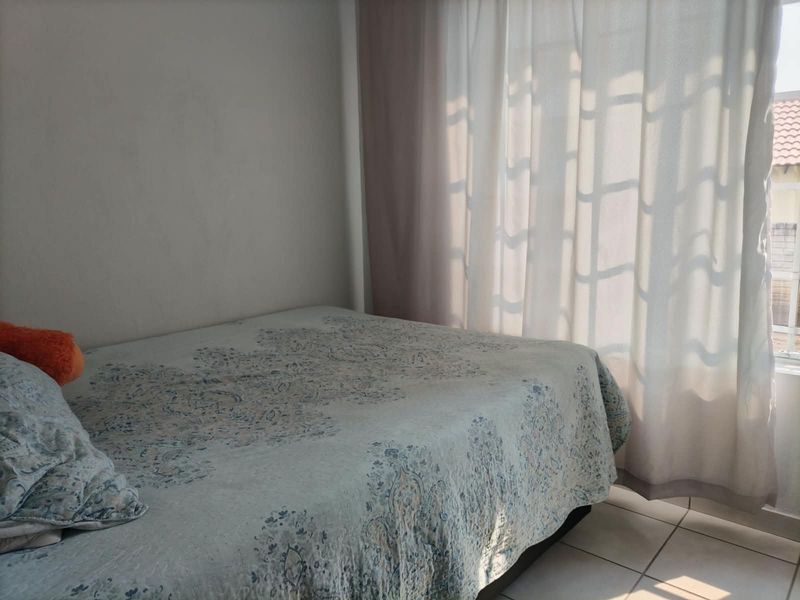 A bedroom featuring tiled flooring and natural light filtering through window curtains.