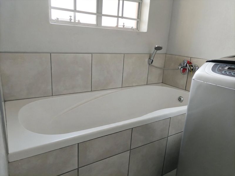 A functional bathroom featuring a built-in bathtub with tiled surround, handheld shower mixer, and a window with security bars.