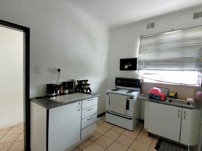A functional kitchen featuring white cabinetry, a freestanding stove, stainless steel sink, and tiled flooring, offering potential for modernization.