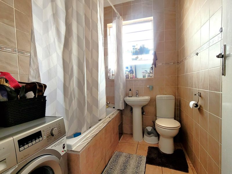 A functional bathroom featuring a pedestal basin, toilet, and a bathtub with a shower curtain, finished with neutral wall and floor tiling.