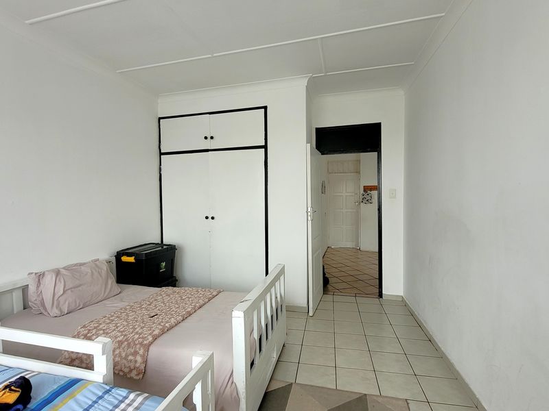 A functional bedroom featuring built-in cupboards, tiled flooring, and coved ceilings, offering a neutral space ready for personalization.