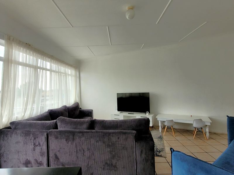A spacious living room featuring tiled flooring, large windows with natural light, and a sliding glass door leading to an outdoor area.