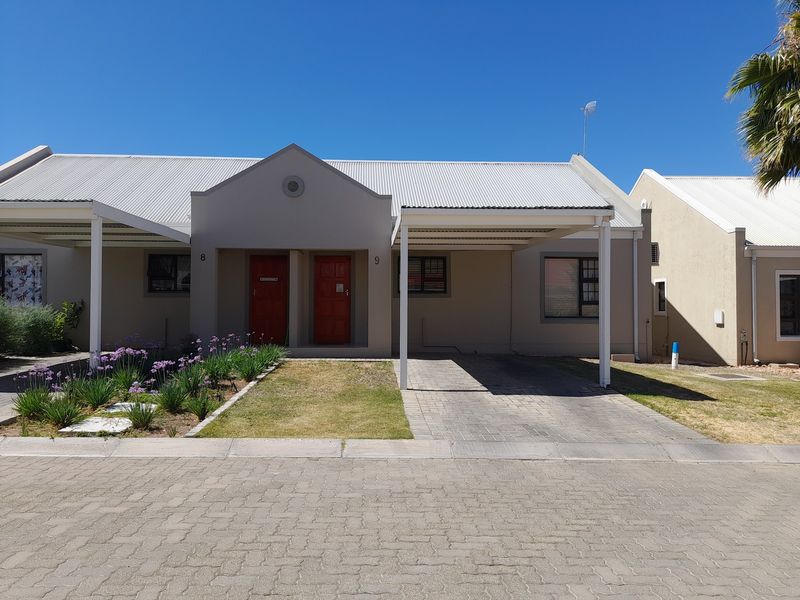 Front elevation of a townhouse featuring a gabled facade, paved driveway, and a covered carport with well-maintained exterior finishes.