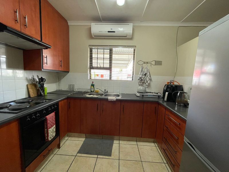 Functional kitchen featuring wood-finish cabinetry, tiled splashbacks, built-in oven and hob, and a wall-mounted air conditioning unit.
