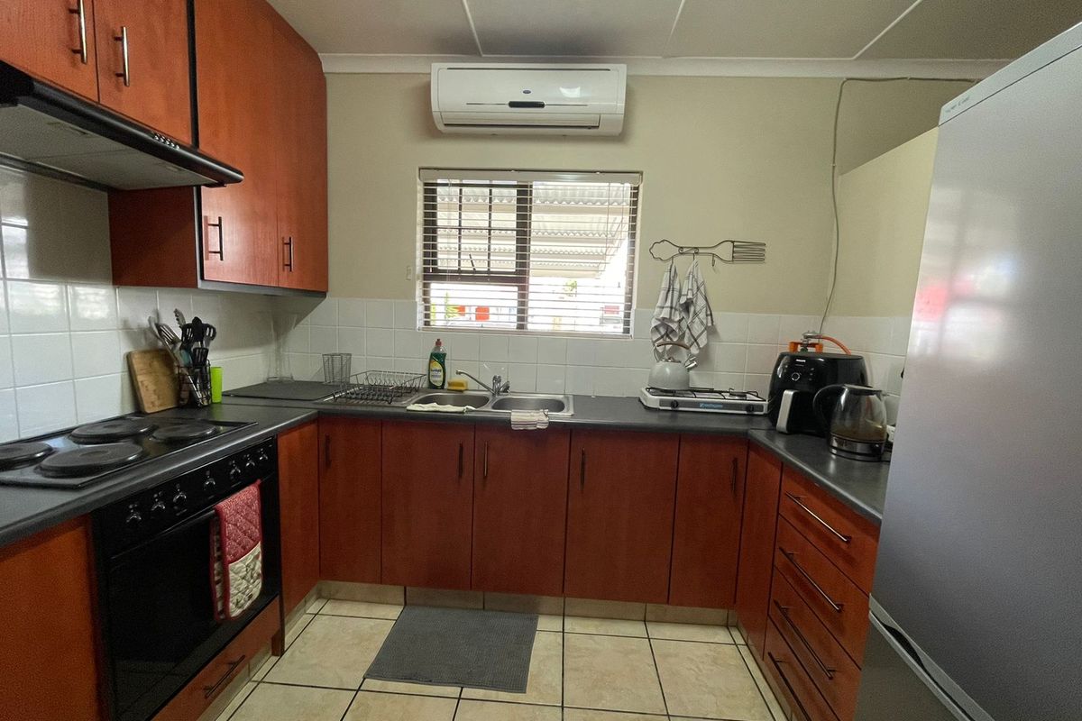 Functional kitchen featuring wood-finish cabinetry, tiled splashbacks, built-in oven and hob, and a wall-mounted air conditioning unit.