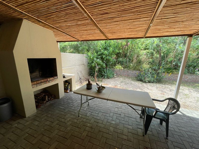 Covered patio area featuring a built-in braai, brick paving, and a bamboo ceiling, overlooking a private garden space.