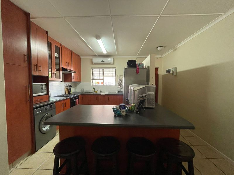 Functional kitchen featuring wood-finish cabinetry, a central island with breakfast bar seating, tiled flooring, and integrated appliances including an oven and extractor fan.