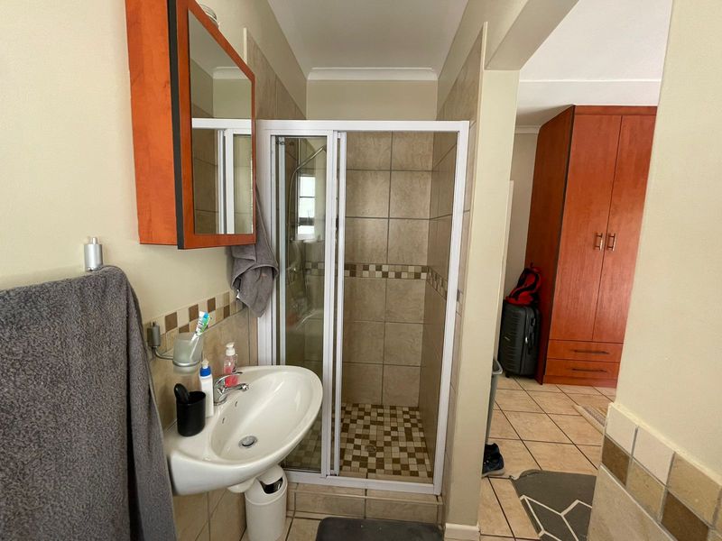 A functional bathroom featuring a shower enclosure, pedestal basin, and wall-mounted vanity cabinet with neutral tiled finishes.